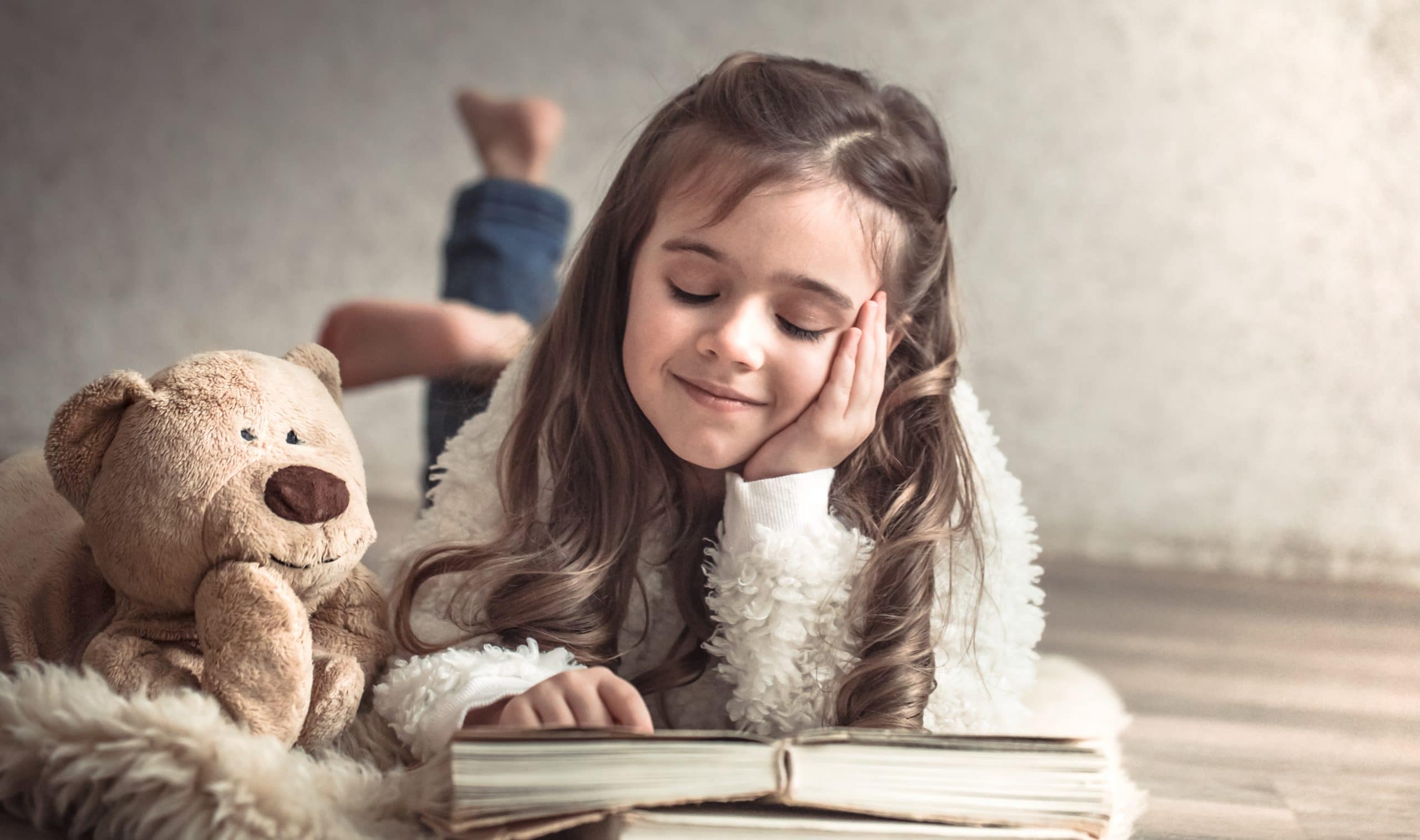 little girl reading a book with a Teddy bear on the floor, concept of relaxation and friendship actividades para hacer con niños leer